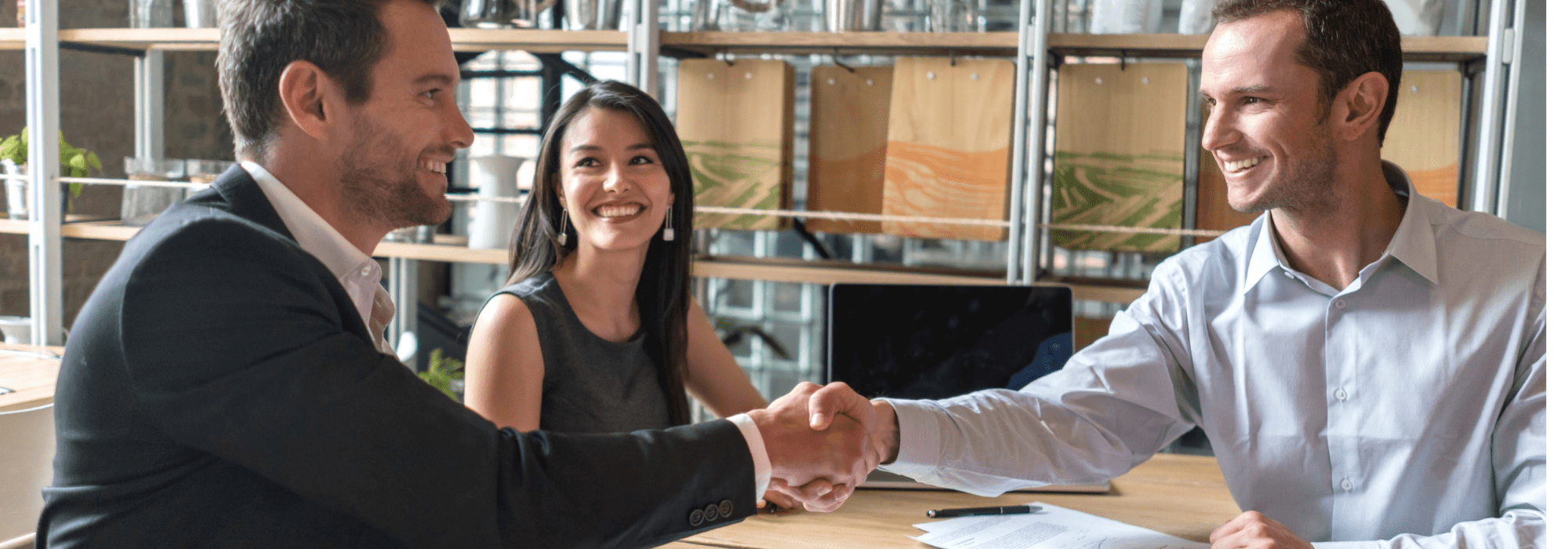 Mężczyzna w marynarce podaje wizytówkę kobiecie w biznesowym ubraniu przy stole