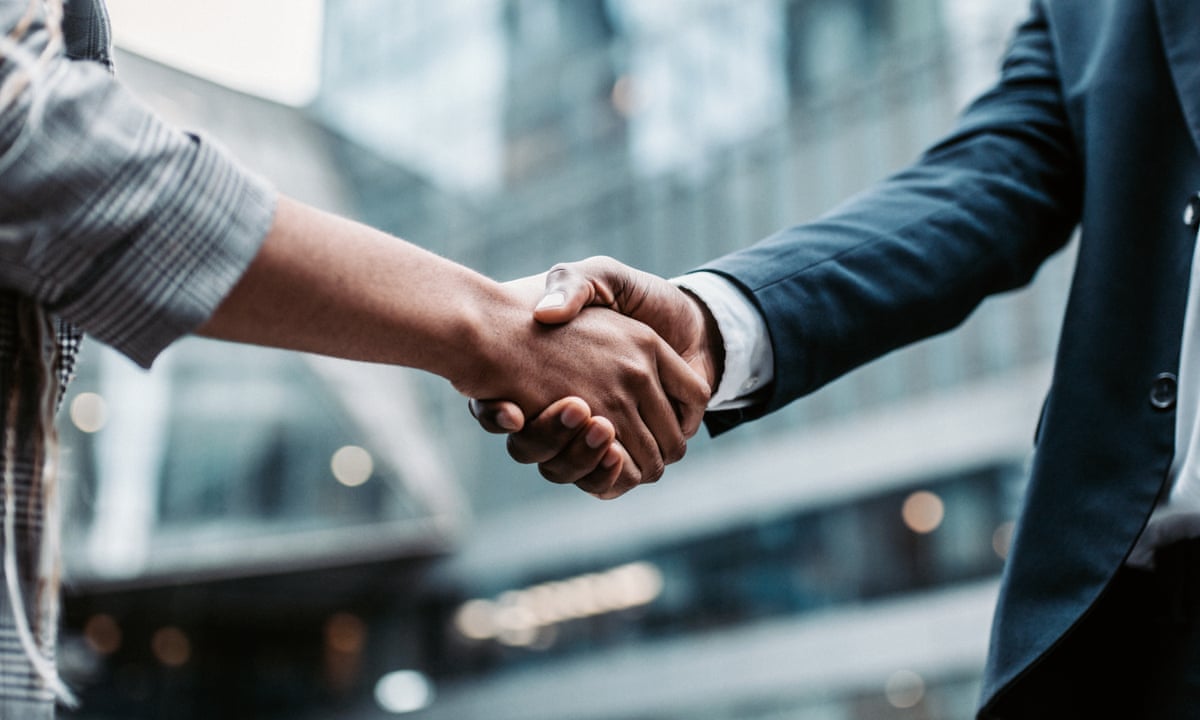 Dwie bizneswomen w żakietach ściskają sobie dłonie na tle city skylinu