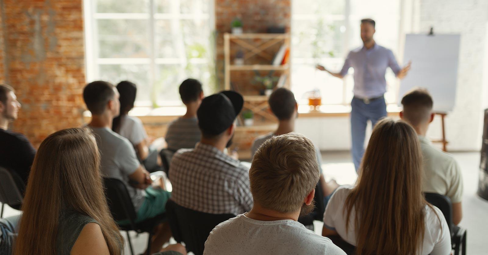 pracownicy notują kluczowe punkty w zeszytach słuchając prezentacji slajdów
